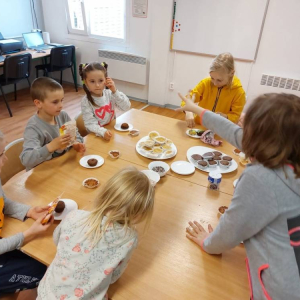 Grupa dzieci siedzących wokół stołu i jedzących. 